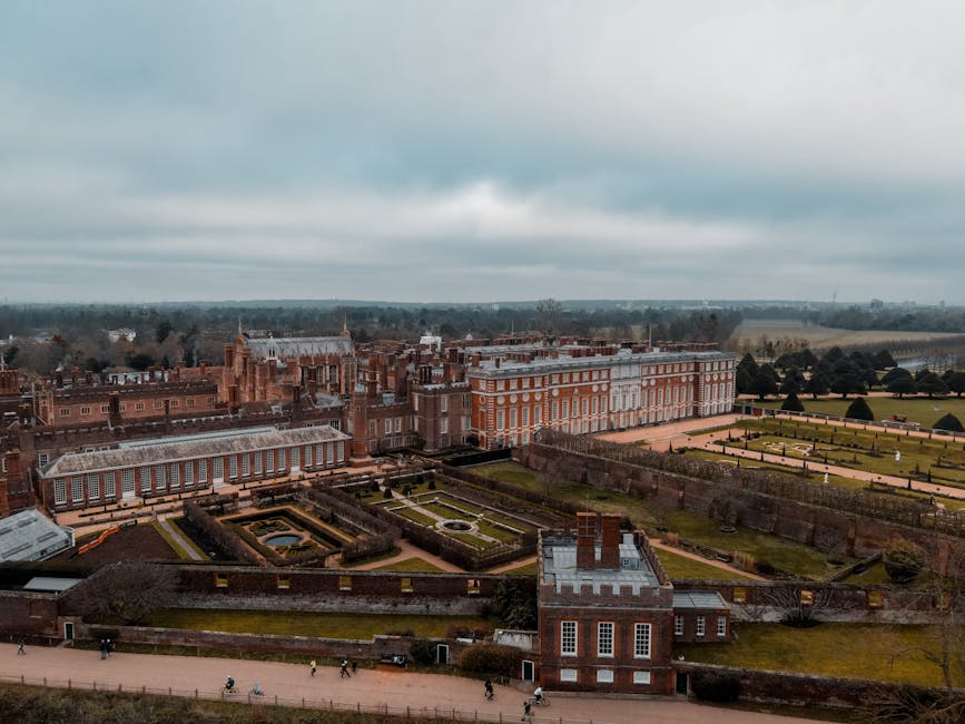 A meticulously maintained garden area featuring a circular design with neatly trimmed boxwood hedges forming a border around a central lawn. Several sculpted, rounded shrubbery plants with dense, dark